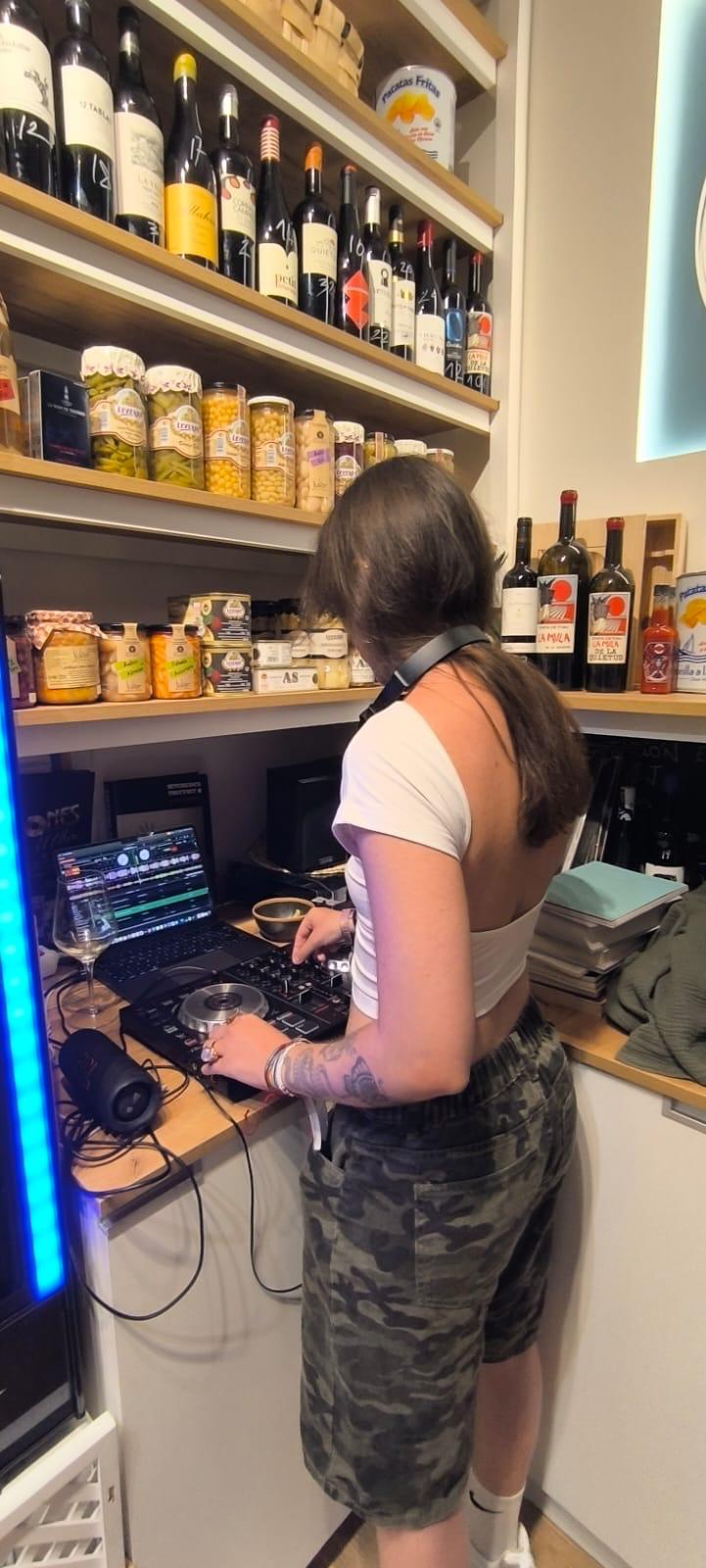 DJ pinchando vinilos junto a las estanterías de vino